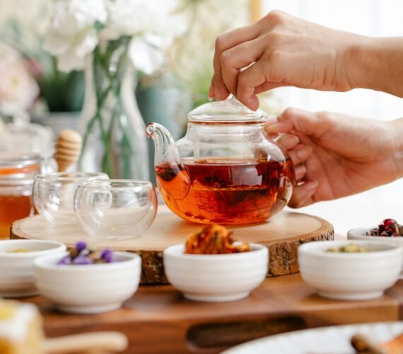 Hands preparing a pot of herbal tea surrounded by dried herbs and cups on a wooden table
